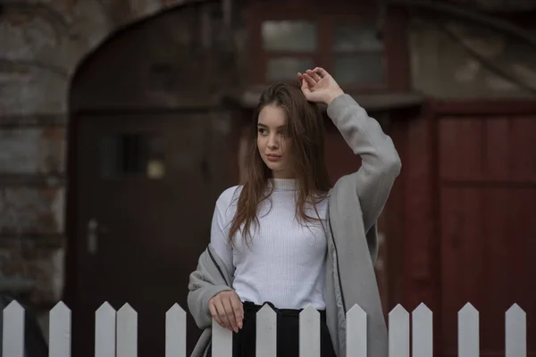 Ung flicka i en grå rock står på bakgrunden av en stadsgata. Flicka i grå rock på en grå bakgrund. — Stockfoto