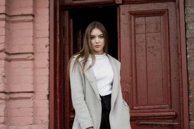 Gri paltolu genç kız bir şehir sokağının arka planında duruyor. Gri arka planda gri ceketli kız..