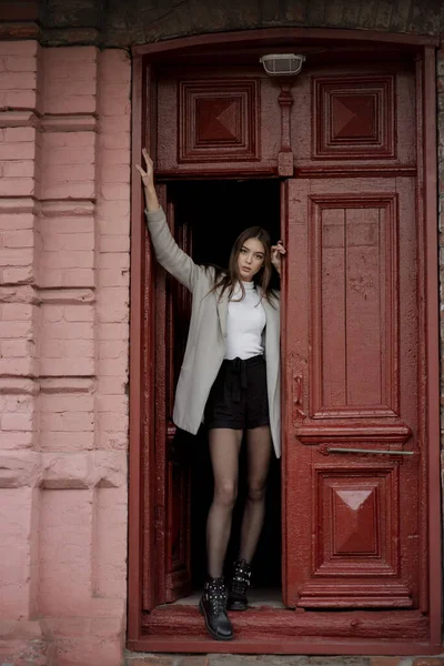 Niña con un abrigo gris se encuentra en el fondo de una calle de la ciudad. Chica en un abrigo gris sobre un fondo gris . —  Fotos de Stock