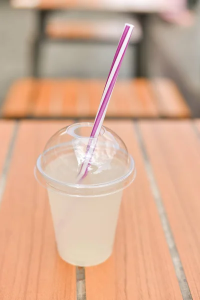Plastic glass of tea lemonade on wooden table. Cold summer drink.