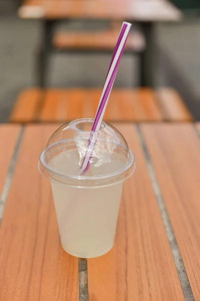 Plastic glass of tea lemonade on wooden table. Cold summer drink.