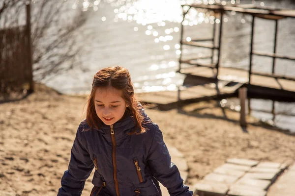 girl on the background of winter lake or river. winter season. Girl in winter clothes on a background of the river. Girl 9 years old against the background of a small river. Teen girl in a blue jacket
