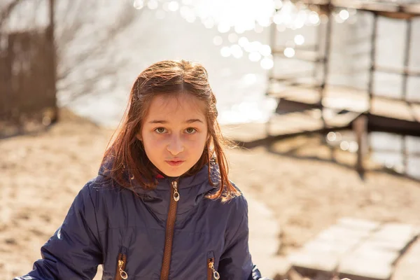 冬の湖や川を背景にした少女です 冬の季節 川の背景に冬服の少女 少女9歳の小さな川の背景に ティーン女の子で青ジャケット — ストック写真