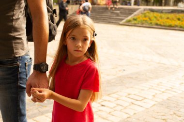 Genç bir adam küçük kızıyla yürüyor, elini onun içinde tutuyor. Baba kızıyla el ele gider. 5-6 yaşlarında bir kız uzun sarı saçlı bir babayla yürüyor. Aile kavramı.