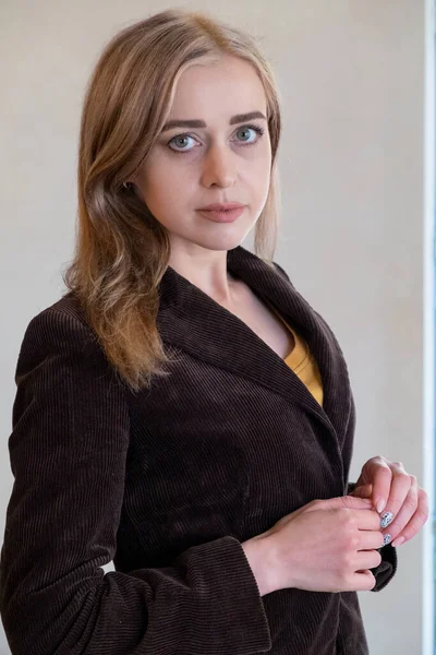 Elegant young woman posing leaning against a white wall. Woman in a classic jacket against a white wall. Elegant young woman posing near a white wall. Office Style. Confident woman