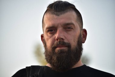 Gün batımında sakallı bir adam. 40 yıllık sakallı bir adamın büyük yüz portresi. Tam yüz portresi. Siyah tişörtlü adam.