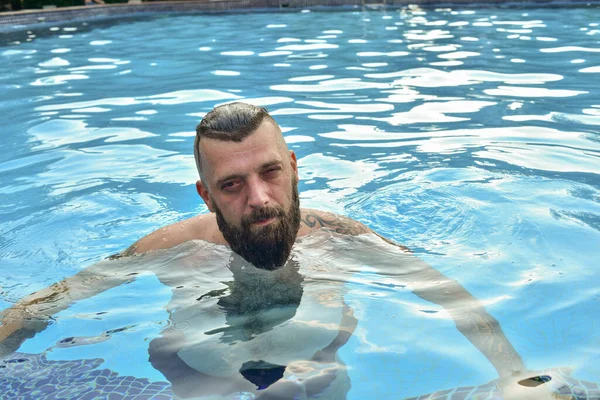 Bearded man swimming in a pool. Man with a beard in the pool. Brunette man on vacation. Summer vacation concept