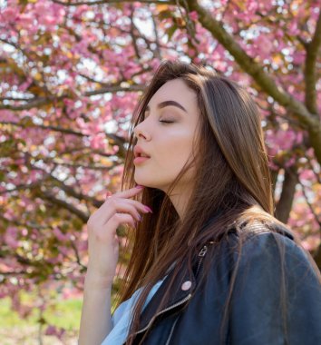 Uzun saçlı güzel bir kız çiçek açan sakura ağacının yanında bahar doğasının güzelliğinin tadını çıkarıyor. Sakura 'da deri ceketli bir kız..