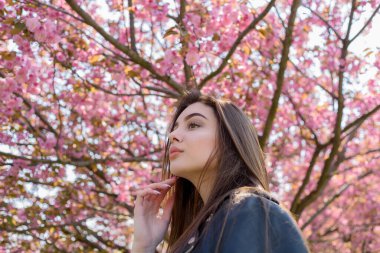 Uzun saçlı güzel bir kız çiçek açan sakura ağacının yanında bahar doğasının güzelliğinin tadını çıkarıyor. Sakura 'da deri ceketli bir kız..