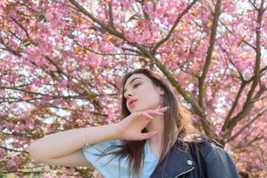 Uzun saçlı güzel bir kız çiçek açan sakura ağacının yanında bahar doğasının güzelliğinin tadını çıkarıyor. Sakura 'da deri ceketli bir kız..