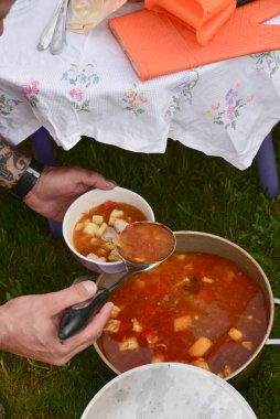 Avludaki kazıkta çorbayla birlikte dökme demir kazan. Yaz günü ve çiçek tarhının yanındaki temiz havada akşam yemeği. Çorba kazıkta bir kazanda hazırlanır. Kazıkta çorba pişirmek.