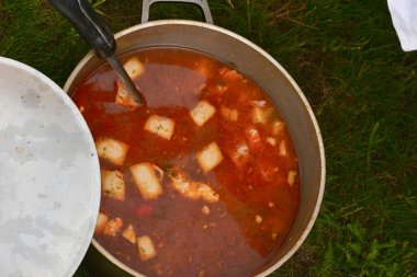 Avludaki kazıkta çorbayla birlikte dökme demir kazan. Yaz günü ve çiçek tarhının yanındaki temiz havada akşam yemeği. Çorba kazıkta bir kazanda hazırlanır. Kazıkta çorba pişirmek.
