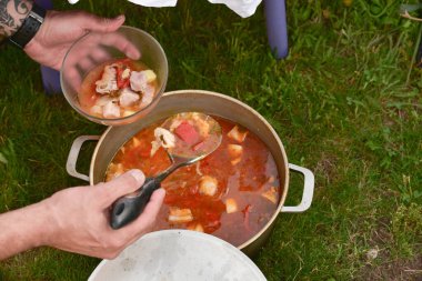 Avludaki kazıkta çorbayla birlikte dökme demir kazan. Yaz günü ve çiçek tarhının yanındaki temiz havada akşam yemeği. Çorba kazıkta bir kazanda hazırlanır. Kazıkta çorba pişirmek.