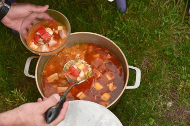 Avludaki kazıkta çorbayla birlikte dökme demir kazan. Yaz günü ve çiçek tarhının yanındaki temiz havada akşam yemeği. Çorba kazıkta bir kazanda hazırlanır. Kazıkta çorba pişirmek.