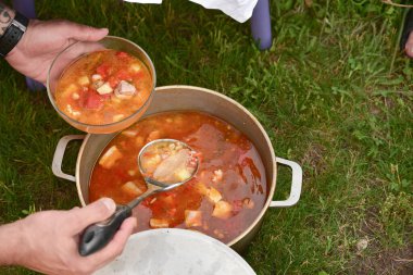 Avludaki kazıkta çorbayla birlikte dökme demir kazan. Yaz günü ve çiçek tarhının yanındaki temiz havada akşam yemeği. Çorba kazıkta bir kazanda hazırlanır. Kazıkta çorba pişirmek.