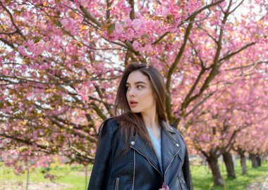 Uzun saçlı güzel bir kız çiçek açan sakura ağacının yanında bahar doğasının güzelliğinin tadını çıkarıyor. Sakura 'da deri ceketli bir kız..