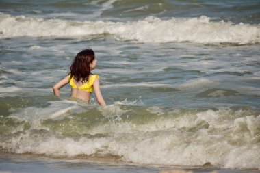 Denizde bir kız. Genç kızın portresi. Gençler için yaz tatili kumları. Güneşli bir gün ve deniz. Çocukluk tatili. Sahilde sarı mayolu bir genç. Gençler denizde yüzer.