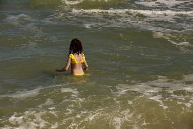 Denizde bir kız. Genç kızın portresi. Gençler için yaz tatili kumları. Güneşli bir gün ve deniz. Çocukluk tatili. Sahilde sarı mayolu bir genç. Gençler denizde yüzer.