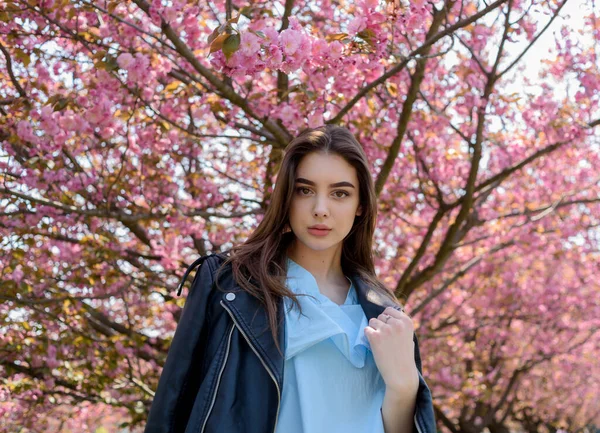 年轻美丽的长发姑娘在盛开的樱花树旁欣赏着春天的自然美景 穿皮夹克的女孩 藏在麻浦 — 图库照片