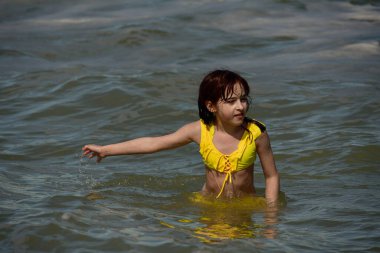 Denizde bir kız. Genç kızın portresi. Gençler için yaz tatili kumları. Güneşli bir gün ve deniz. Çocukluk tatili. Sahilde sarı mayolu bir genç. Gençler denizde yüzer.