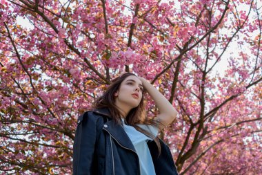 Uzun saçlı güzel bir kız çiçek açan sakura ağacının yanında bahar doğasının güzelliğinin tadını çıkarıyor. Sakura 'da deri ceketli bir kız..