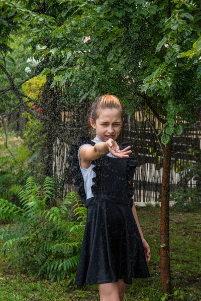 Wet schoolgirl standing in the rain. girl wet. teenager in school uniform in spring or warm autumn. Girl 5th grade. Hair coloring. Portrait of a schoolgirl with splashes of water. Back to school