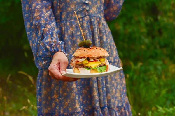 Juicy burger. A burger in the hands of a woman. Breakfast concept, Shopkeeper\'s market photo, Delicious food concept, Fast food concept, Food and drink. Hand holding a tasty fast food cheeseburger.