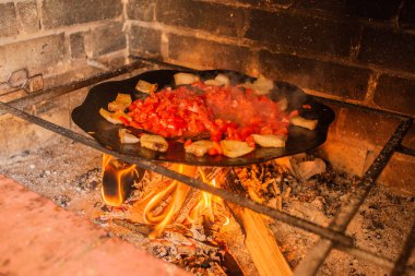 Domates ve domuz yağı ateşte. Pastırma ve domates dilimleri ateşte tavada kızartılır. Kızarmış pastırma