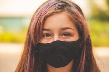 Genç bir kız, koronavirüs hastalığına karşı koruyucu bir maske takıyor. Antiviral maskeli bir gencin yakın çekimi. Dışarıda koruyucu maskeli bir kız. Salgın, virüs, koronavirüs
