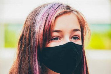 Genç bir kız, koronavirüs hastalığına karşı koruyucu bir maske takıyor. Antiviral maskeli bir gencin yakın çekimi. Dışarıda koruyucu maskeli bir kız. Salgın, virüs, koronavirüs
