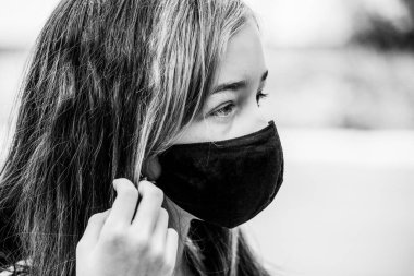 Genç bir kız, koronavirüs hastalığına karşı koruyucu bir maske takıyor. Antiviral maskeli bir gencin yakın çekimi. Dışarıda koruyucu maskeli bir kız. Salgın, virüs, koronavirüs