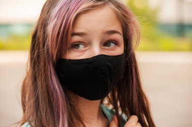 Genç bir kız, koronavirüs hastalığına karşı koruyucu bir maske takıyor. Antiviral maskeli bir gencin yakın çekimi. Dışarıda koruyucu maskeli bir kız. Salgın, virüs, koronavirüs