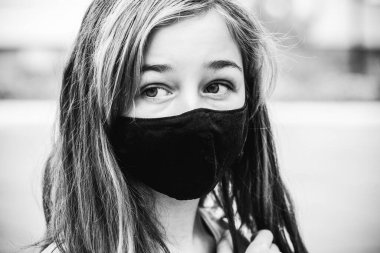 Genç bir kız, koronavirüs hastalığına karşı koruyucu bir maske takıyor. Antiviral maskeli bir gencin yakın çekimi. Dışarıda koruyucu maskeli bir kız. Salgın, virüs, koronavirüs