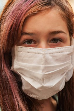 Genç bir kız, koronavirüs hastalığına karşı koruyucu bir maske takıyor. Antiviral maskeli bir gencin yakın çekimi. Dışarıda koruyucu maskeli bir kız. Salgın, virüs, koronavirüs