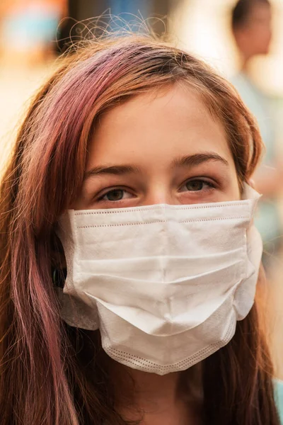 A young girl wears a face mask that protects against the spread of coronavirus disease. Close- up of teenager in an antiviral mask. Girl in a protective mask outdoors. Pandemic, virus, coronavirus