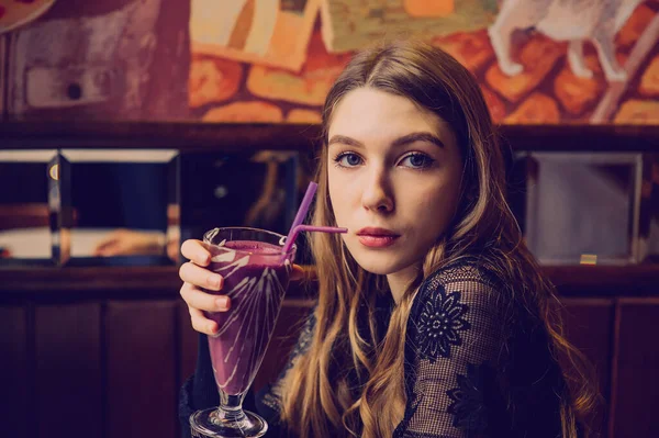 Beautiful Young Woman with Fruit smoothie. Girl drinking smoothie in a cafe. Girl in black dress. A girl with natural hair. Girl and relaxation in a cafe, healthy food, vitamins. Calm concept