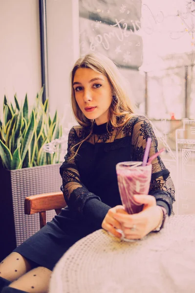 Meyveli buzlu güzel genç bayan. Kafede smoothie içen bir kız. Siyah elbiseli kız. Doğal saçlı bir kız. Kız ve kafede rahatlama, sağlıklı yiyecekler, vitaminler. Sakin kavram