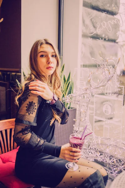 Meyveli buzlu güzel genç bayan. Kafede smoothie içen bir kız. Siyah elbiseli kız. Doğal saçlı bir kız. Kız ve kafede rahatlama, sağlıklı yiyecekler, vitaminler. Sakin kavram