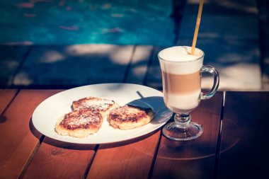 Havuz kenarında kahvaltı için bir fincan latte ve sıcak cheesecake. Sağlıklı kahvaltı, kahve, kapuçino.