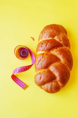 Şerit mezura ve sarı arka planda haşhaş tohumlu çörek. Sağlıklı gıda, diyet, kilo kaybı ve zayıflık kavramı. Boşluğu kopyala.