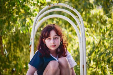 Güzel esmer bir kızın açık hava portresi. Kız çocukların kaydırağından kayıyor. Yazın 9-10 yaşlarında.