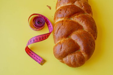 Şerit mezura ve sarı arka planda haşhaş tohumlu çörek. Sağlıklı gıda, diyet, kilo kaybı ve zayıflık kavramı. Boşluğu kopyala.