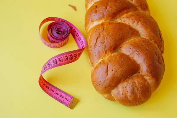 Şerit mezura ve sarı arka planda haşhaş tohumlu çörek. Sağlıklı gıda, diyet, kilo kaybı ve zayıflık kavramı. Boşluğu kopyala.