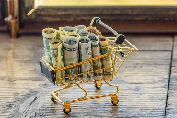 Supermarket grocery push cart for shopping with bundle of dollars money banknote cash. Dollars in the cart. Finance concept