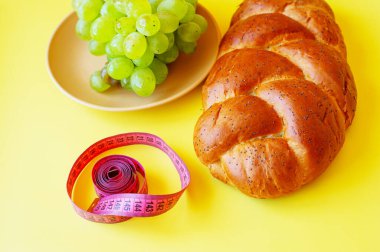 Şerit mezura, üzüm ve sarı arka planda haşhaş tohumlu çörek. Sağlıklı gıda, diyet, kilo kaybı ve zayıflık kavramı. Üzüm, diyet, sağlıklı yiyecekler, vitaminler