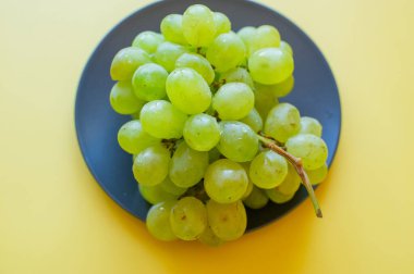 Siyah bir tabakta yeşil üzümler. Sarı arka planda üzümler. vitamin