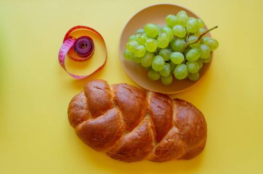 Şerit mezura ve sarı arka planda haşhaş tohumlu çörek. Sağlıklı gıda, diyet, kilo kaybı ve zayıflık kavramı. Tabakta üzümler
