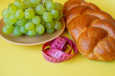 Şerit mezura ve sarı arka planda haşhaş tohumlu çörek. Sağlıklı gıda, diyet, kilo kaybı ve zayıflık kavramı. Tabakta üzümler