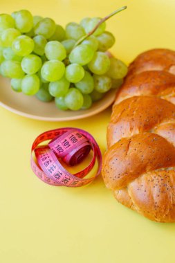 Şerit mezura ve sarı arka planda haşhaş tohumlu çörek. Sağlıklı gıda, diyet, kilo kaybı ve zayıflık kavramı. Tabakta üzümler