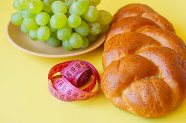 Şerit mezura ve sarı arka planda haşhaş tohumlu çörek. Sağlıklı gıda, diyet, kilo kaybı ve zayıflık kavramı. Tabakta üzümler
